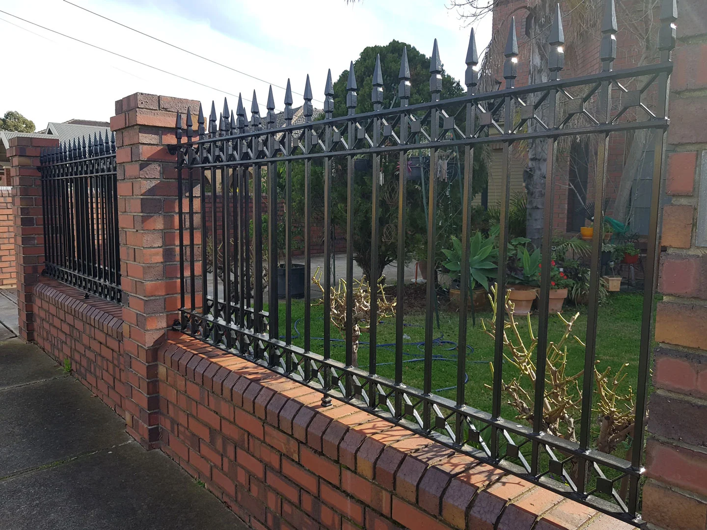 Spear-top wrought iron fence mounted on a brick wall