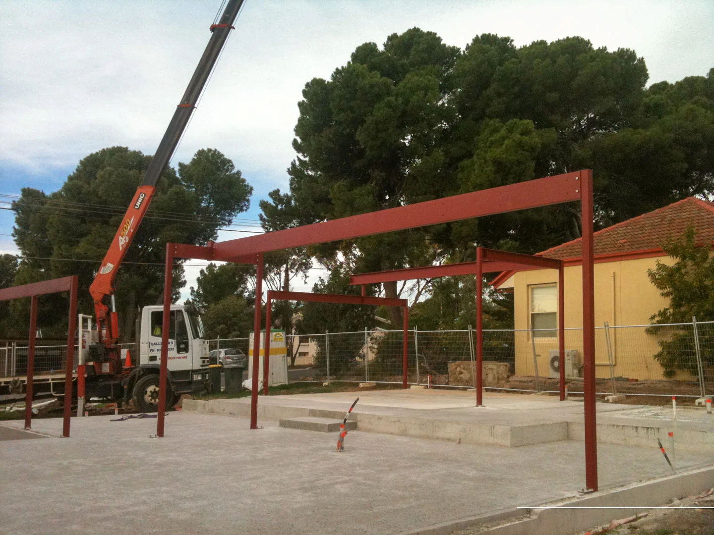 Crane lifting steel beams over a residential frame